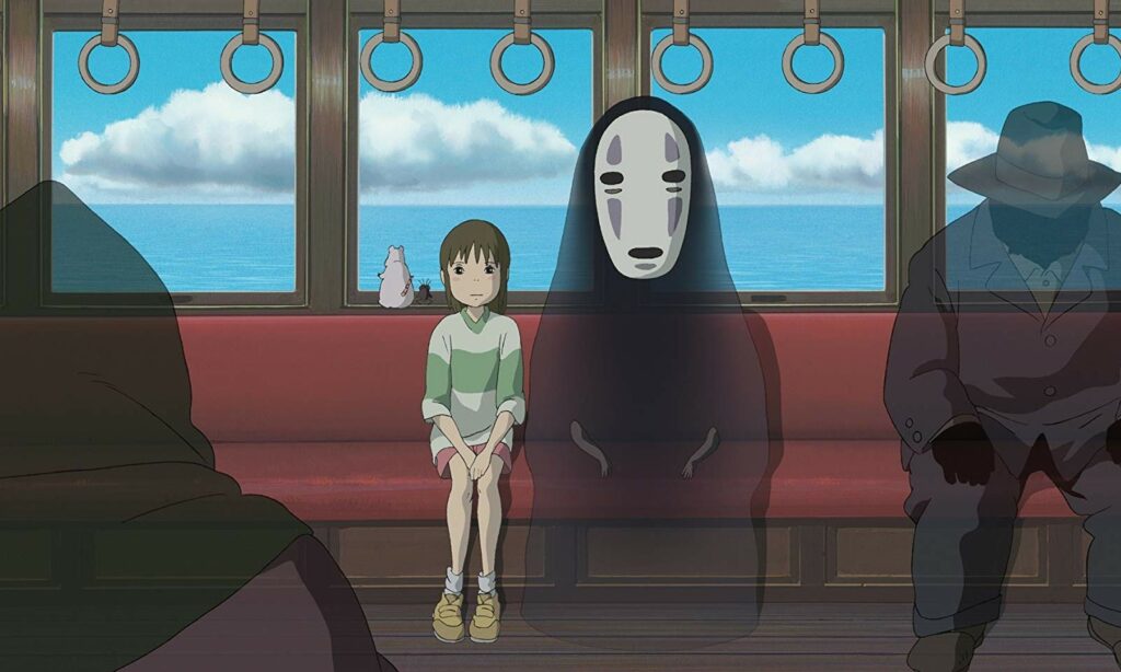 Chihiro est assise dans un train à côté d'un monstre noir qui porte un masque blanc. Un hamster et un insecte est à sa droite.
